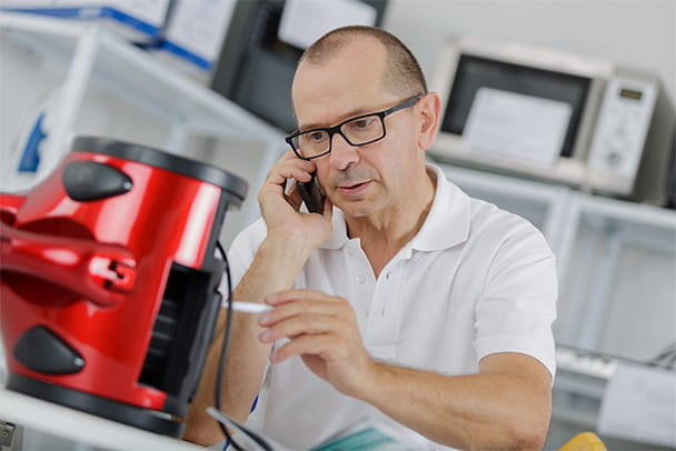 Ein Mann telefoniert während einer Reparatur eines Geräts in seiner Werkstatt im Firmenquartier